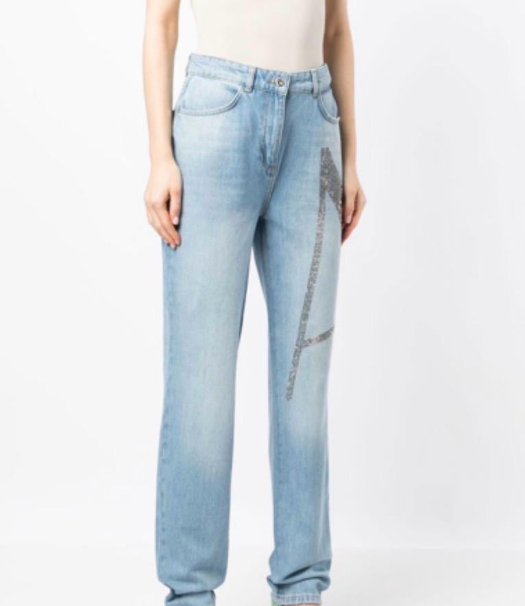 I jeans in denim azzurro chiaro caratterizzato da una grande decorazione a forma di lettera "A" realizzata con strass o pietre luccicanti sulla gamba sinistra.
Questo specifico design con decorazione a gioiello